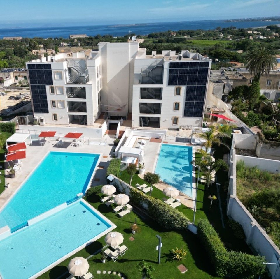 Ein Hotel mit mehreren Schwimmbecken, Liegestühlen und Meerblick.