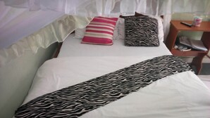 Un lit bien fait, avec une literie blanche, un plaid à motifs zébrés et deux oreillers (un à rayures et l’autre à motifs zébrés).