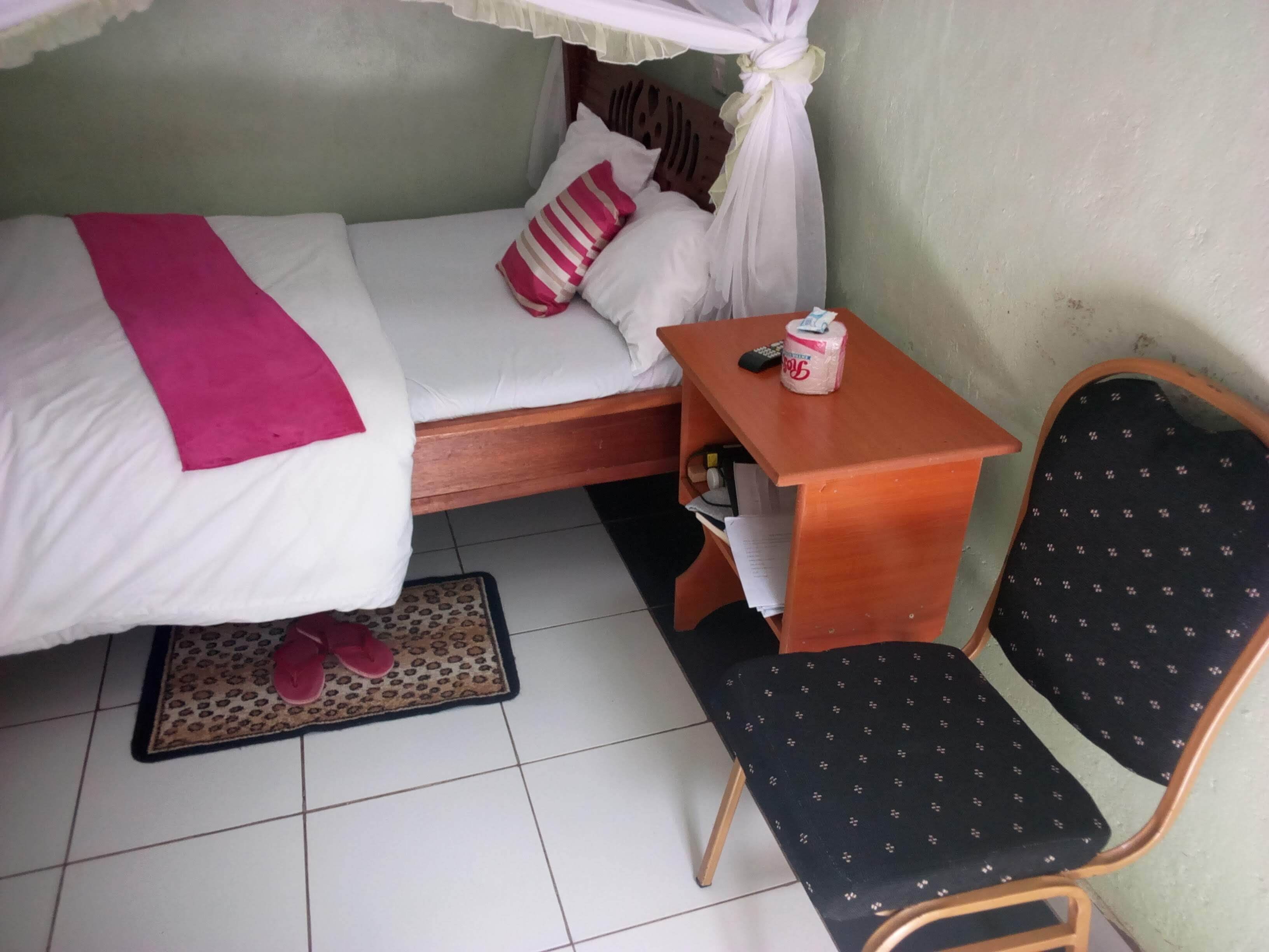 Une petite pièce, bien rangée, comprenant un lit, une chaise, une table de chevet et une petite table.