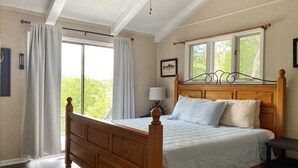Una camera da letto con un letto in legno, una finestra con tende, una ventola a soffitto e un quadro appeso al muro.