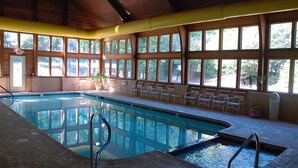 Una piscina interna con ampie vetrate, sedie e soffitto in legno.