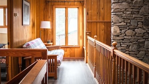 Un interno in legno con parete in pietra, panche di legno, un letto con coperta a quadri e una finestra vista.