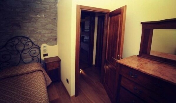 Un dormitorio con cama, cómoda de madera, mesita de noche y pared de piedra.