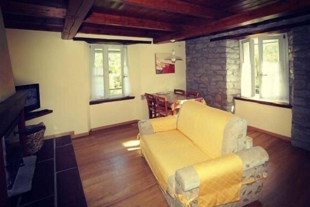 Una sala de estar acogedora con un sofá amarillo, suelo de madera, paredes de piedra y ventanas grandes.