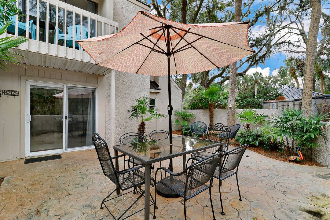 Une terrasse extérieure avec une table et des chaises en verre, un parasol à motifs et une vue sur un immeuble d’habitation.