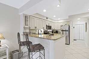 A modern kitchen with white cabinetry, a granite countertop, stainless steel appliances, and a bar stool seating area.