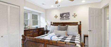 Un dormitorio con una cama de madera, un ventilador de techo, una ventana y una puerta.