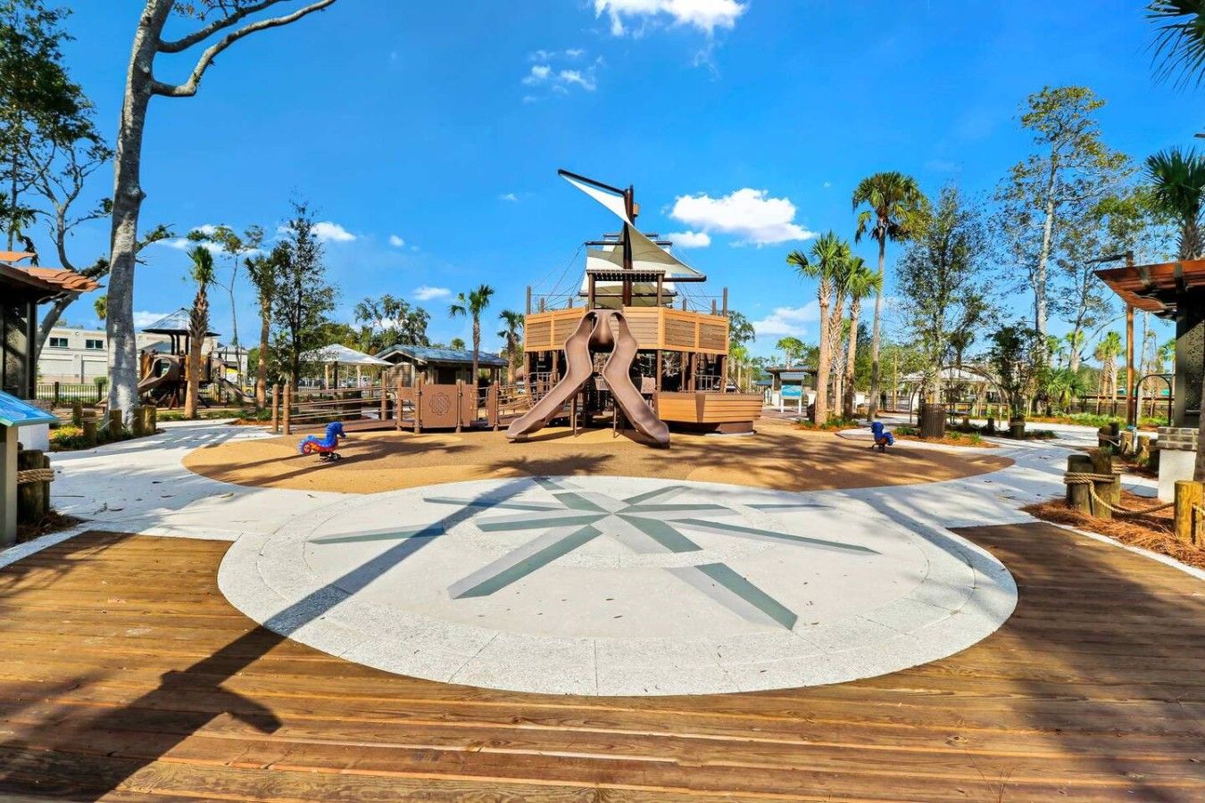 Een speeltuin met een glijbaan en klimconstructies, omringd door palmbomen en een heldere lucht.