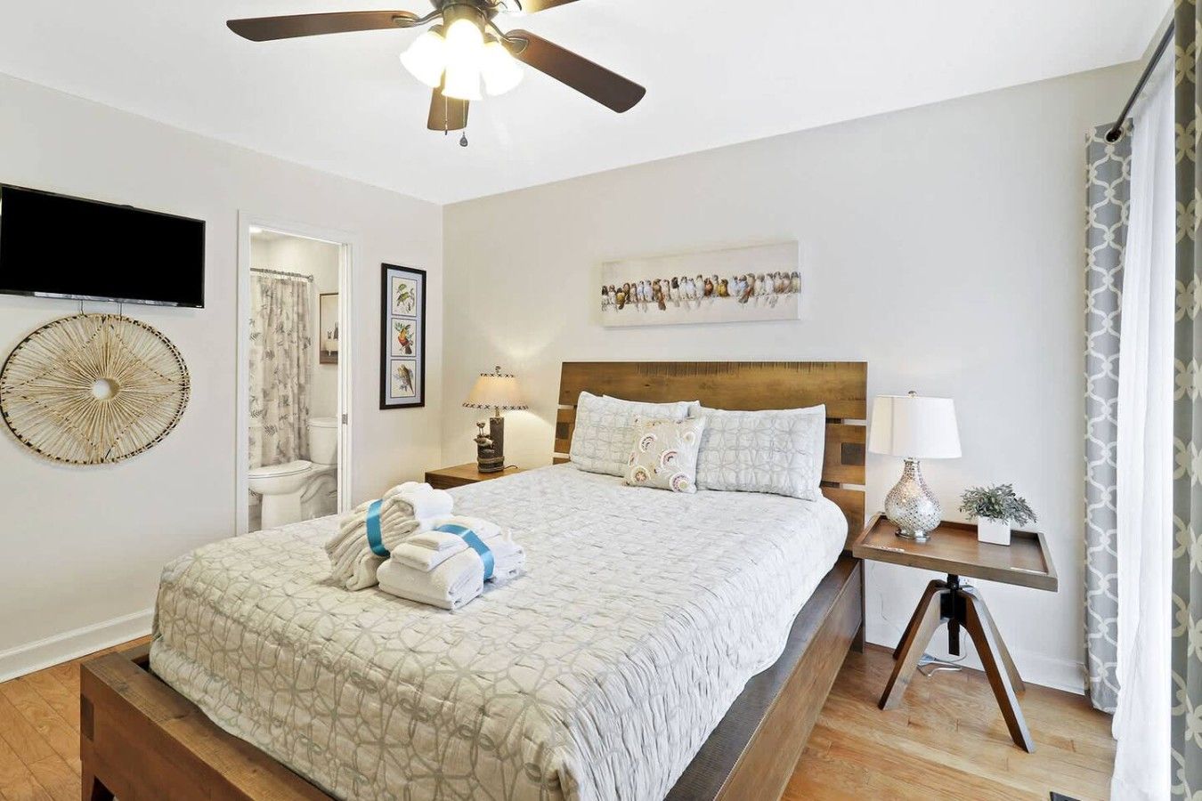 A neatly arranged bedroom with a bed, bedside tables, a ceiling fan, and a wall-mounted TV.