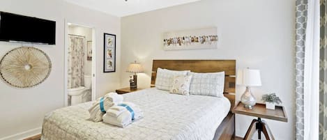 A neatly arranged bedroom with a bed, bedside tables, a ceiling fan, and a wall-mounted TV.