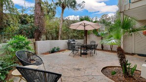 Un patio exterior con una mesa, sillas, una parrilla y un gran paraguas.