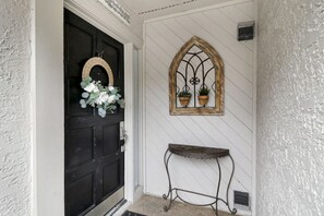 A black door with a wreath, a decorative window with plants, and a metal bench.