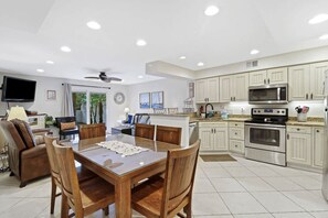 A spacious kitchen with white cabinetry, a dining area with a wooden table and chairs, and a ceiling fan.