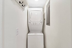 Un lavadero pequeño con lavadora y secadora, una ventana y un interruptor de luz en la pared.