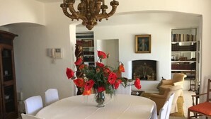 Una sala da pranzo con un tavolo rotondo, sedie bianche, un lampadario e un vaso di fiori rossi.