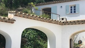Un edificio bianco con tetto in tegole e finestre ad arco. Si notano piante in vaso e un muro in pietra.