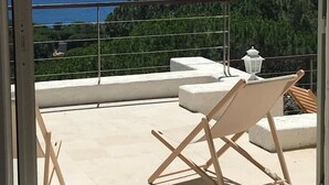 Un balcone con vista sul mare, un tavolo bianco e una sedia di legno.