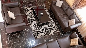 A modern living room with a large flat-screen TV, multiple sofas, a coffee table, and a patterned rug. - Mays Haven (Taifa)