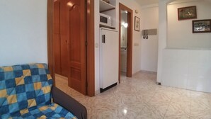 A room with a checkered sofa, a wooden door, a white refrigerator, and a tiled floor. - Colera Apartment A costa brava (Colera)