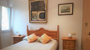 A bedroom with a wooden bed, two bedside tables, a nightstand, a window, and two framed pictures on the wall. - Colera Apartment A costa brava (Colera)