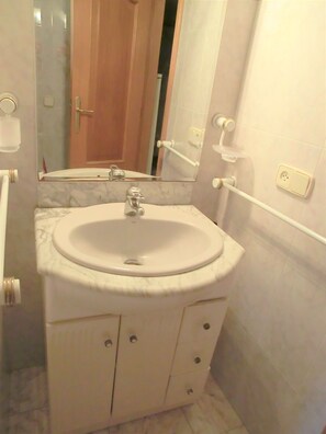 A bathroom with a white sink, marble countertop, and a mirror above it. There are two drawers below the sink and a door leading to another room.