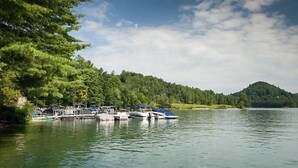 A lakeside dock with boats and a forested hill in the background. - Luxurious Villas in the Blue Ridge Mountains. (Cashiers)