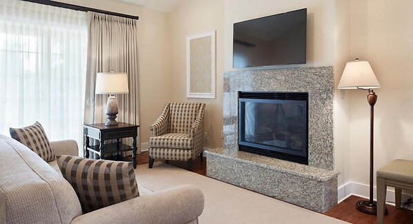 A living room with a fireplace, a sofa, a chair, a TV mounted above the fireplace, and a floor lamp. - Luxurious Villas in the Blue Ridge Mountains. (Cashiers)