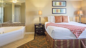 A hotel room with a large bed, a separate bathroom with a bathtub, two bedside lamps, and two abstract paintings on the wall. - Amazing Resort close to Disney World in the Sunshine State! (Orlando)