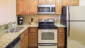 A kitchen with granite countertops, wooden cabinets, a stainless steel refrigerator, a built-in oven, a microwave, and a dishwasher. - Amazing Resort close to Disney World in the Sunshine State! (Orlando)