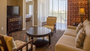A hotel room with a sofa, two armchairs, a small table, a TV on a cabinet, and a window with curtains. - Amazing Resort close to Disney World in the Sunshine State! (Orlando)
