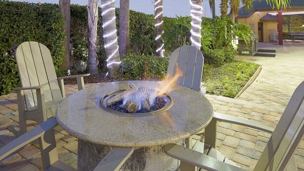 A round stone table with a fire pit in the center, surrounded by two Adirondack chairs. - Amazing Resort close to Disney World in the Sunshine State! (Orlando)