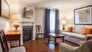 A living room with a fireplace, a sofa, a coffee table, and a television. - Historic Patrick Henry Square Resort (Williamsburg)
