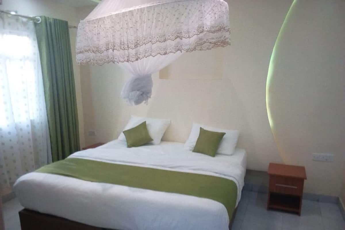 Un dormitorio con cama, almohadas verdes, dosel blanco, mesita de noche y cortina verde.