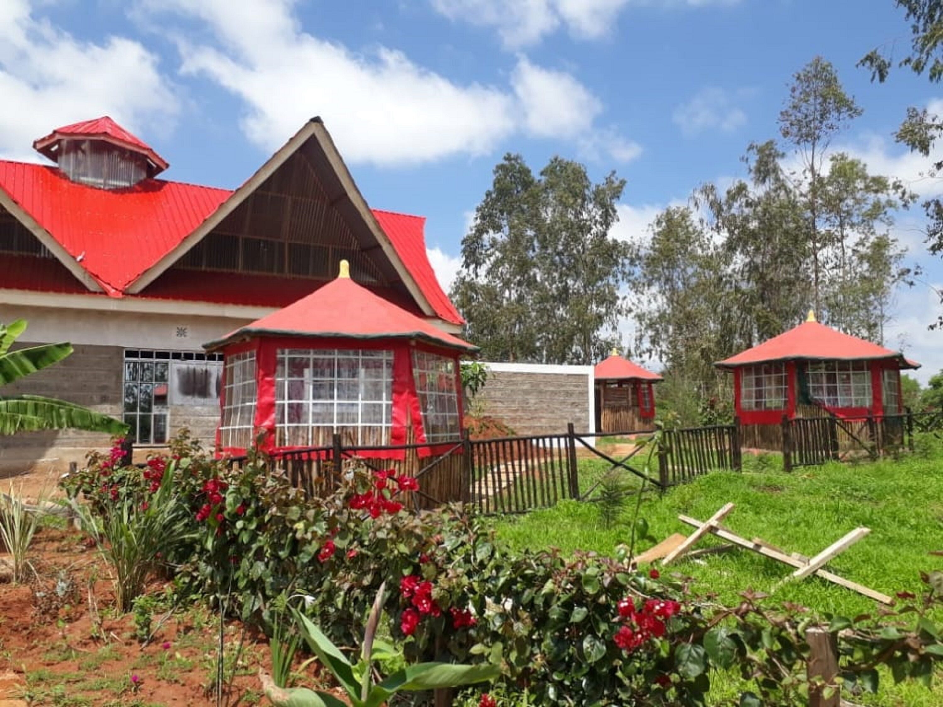Un bâtiment doté d’un toit rouge et de plusieurs petites constructions également coiffées de toits rouges, le tout entouré de verdure et d’une clôture.