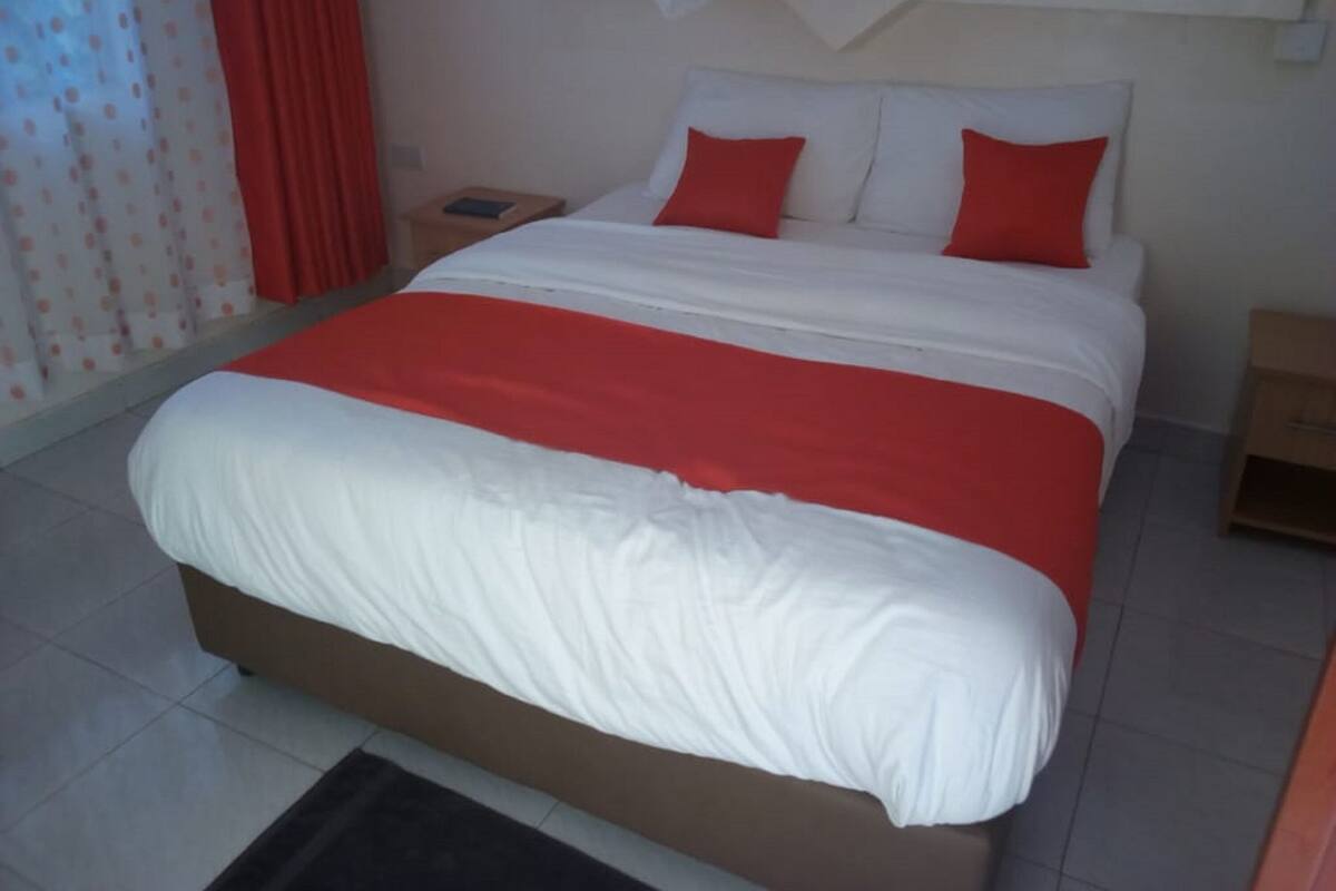 Una cama bien hecha con ropa de cama blanca y roja, una mesita de noche de madera y una pequeña mesilla.