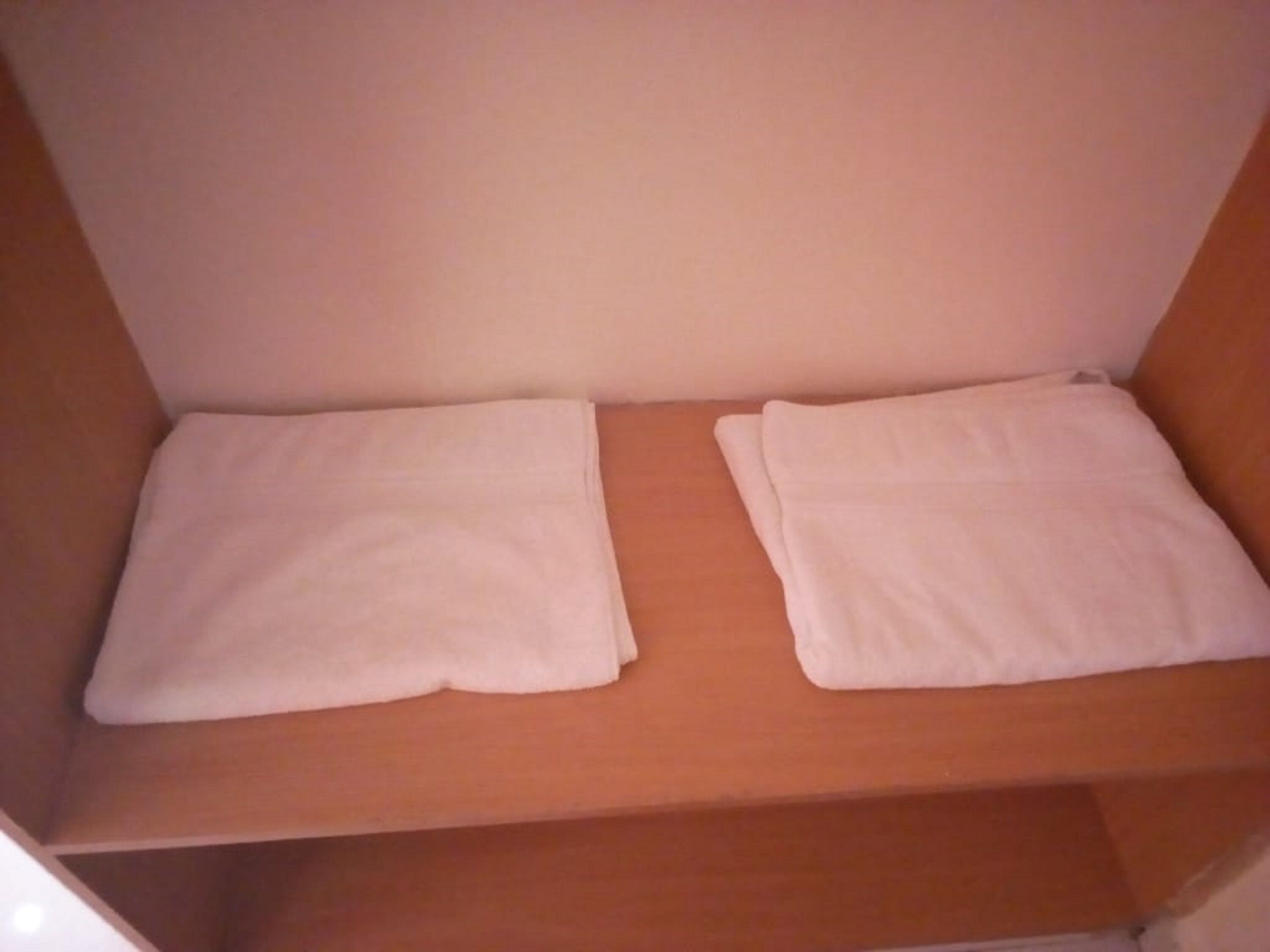 Una habitación pequeña con una cama individual, paredes blancas lisas y un cabecero sencillo.