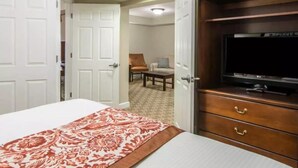 A hotel room with a bed, a TV on a wooden cabinet, and a chair in the background. - Historic Patrick Henry Square Resort (Williamsburg)