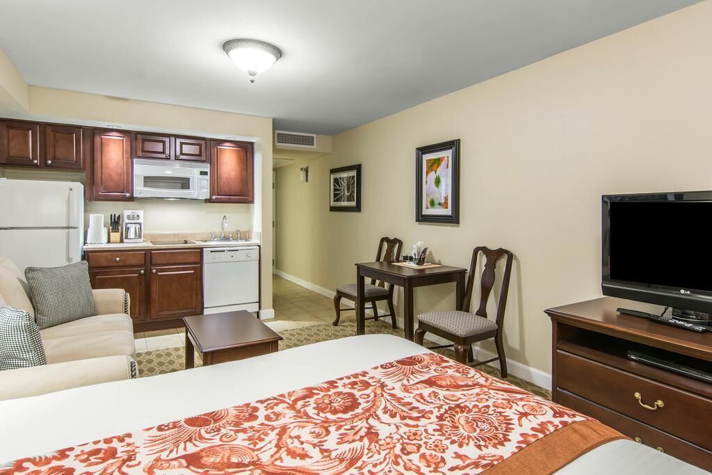 A hotel room with a bed, a TV, a kitchenette, and a dining area.