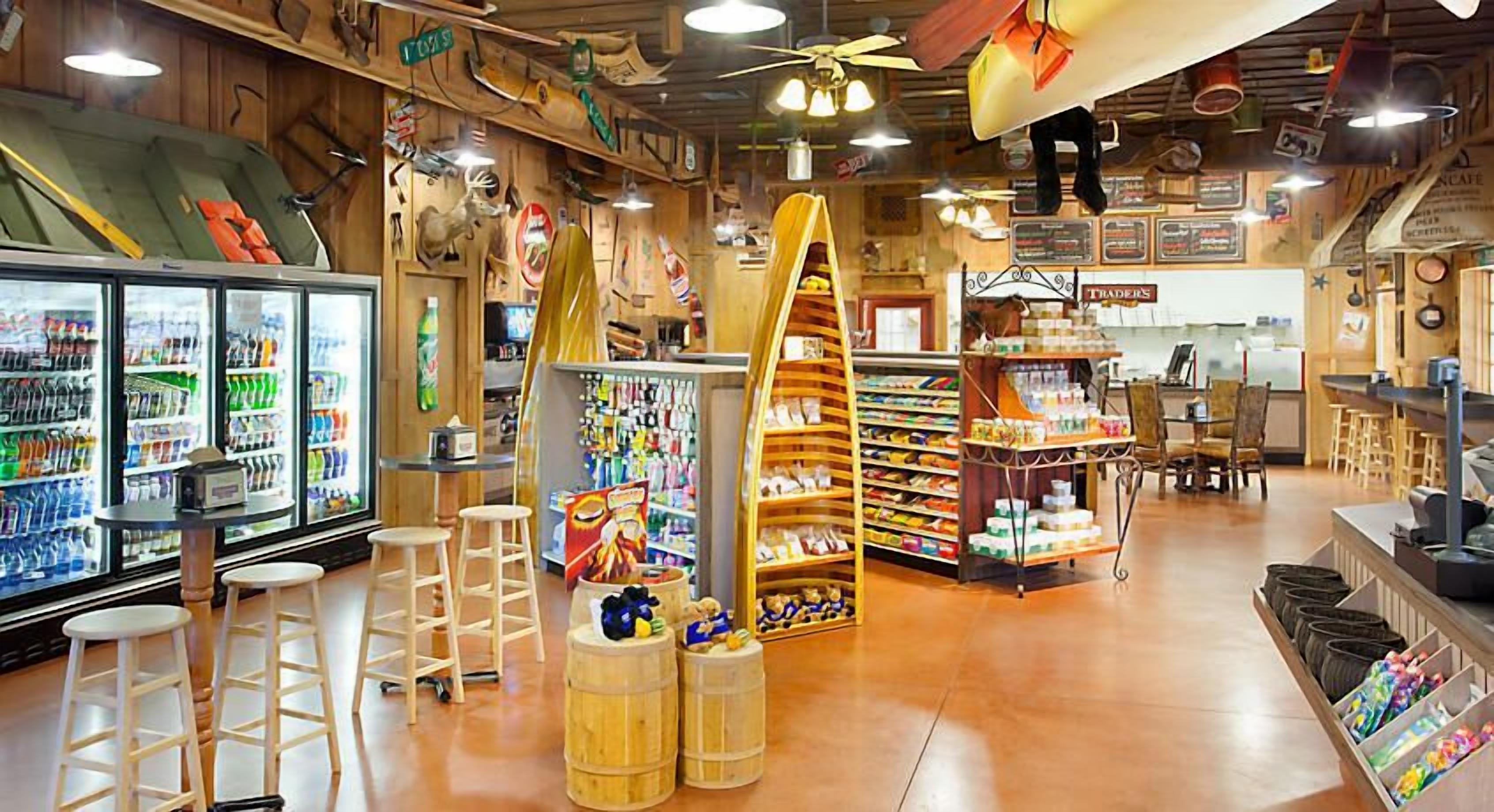 Interior de una tienda con estantes llenos de diversos productos, un refrigerador y taburetes de madera.