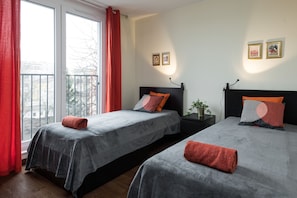 A bedroom with two beds, red curtains, and two framed pictures on the wall.