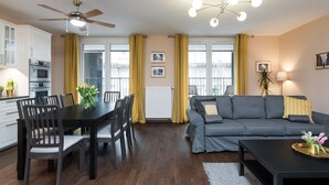 A modern living room with a grey sofa, a dining table with chairs, a black coffee table, and a ceiling fan.