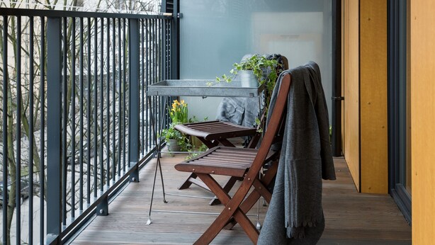 A balcony with a table and chairs, a potted plant, and a view of the city.