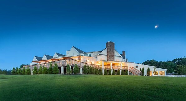 A large, modern house with multiple levels and a prominent chimney, surrounded by a well-maintained lawn.
