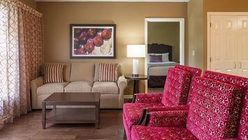 Un salon avec un canapé beige, un canapé rouge à motifs, une table basse en bois et un tableau encadré accroché au mur.