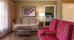 Una sala de estar con un sofá color beige, un sofá rojo con estampado, una mesa de centro de madera y un cuadro en la pared.