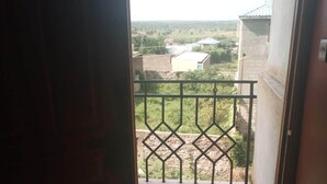 An open door leading to a balcony with a metal railing, a tiled floor, and a view of a residential area with houses and greenery. - Sirlo Hotel (Thika)