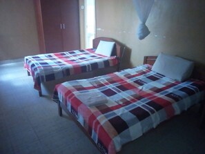Two single beds with checkered bedding in a room with a wardrobe and a window. - Sirlo Hotel (Thika)