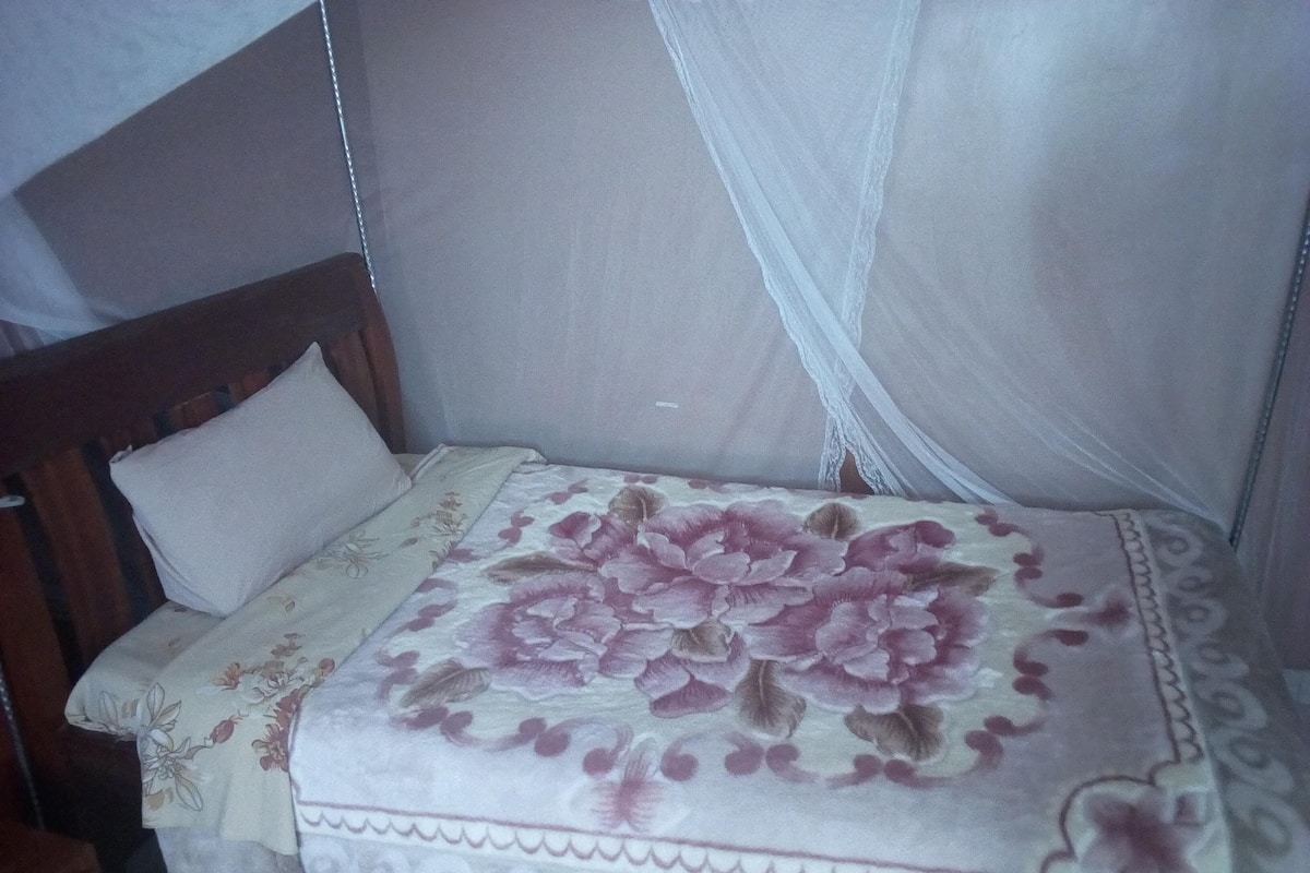 A bed with a floral bedspread, a wooden headboard, and a white mosquito net.