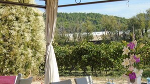 An outdoor dining area with wicker chairs, a table set with wine glasses, menus, and a decorative flower arrangement. - Le Moulin de Lavon (Gargas)