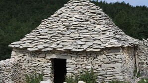 A stone hut with a conical roof, surrounded by rocks and greenery. - Le Moulin de Lavon (Gargas)